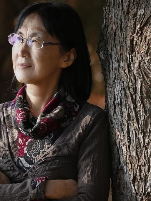 Noriko Kawakami mit verschränkten Armen an einen Baum gelehnt