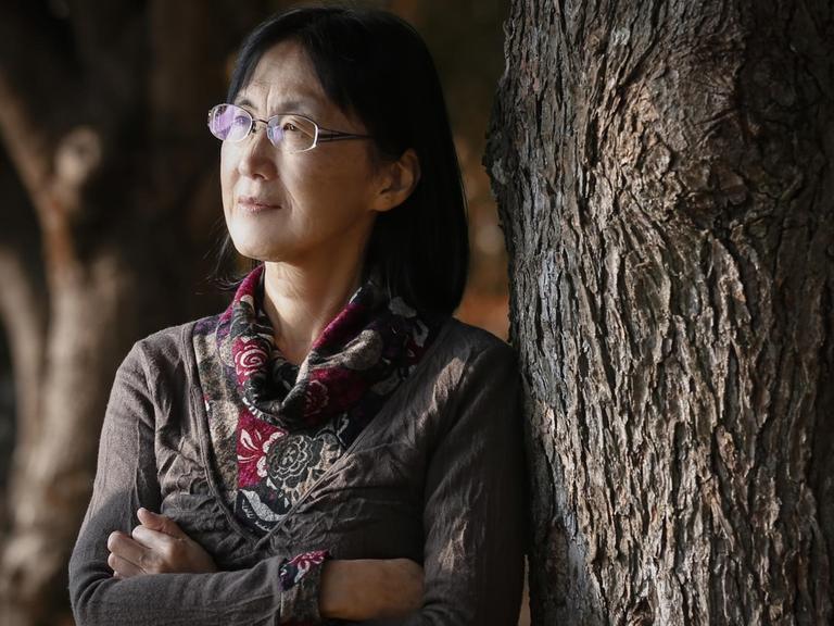Noriko Kawakami mit verschränkten Armen an einen Baum gelehnt
