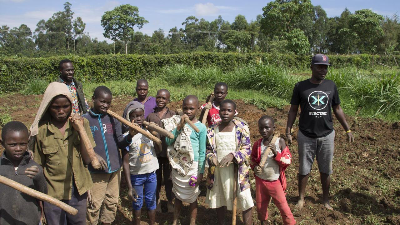 Eine Gruppe von afrikanischen Jungen und ihr Sozialarbeiter mit Gartengeräten im Gemüsegarten.