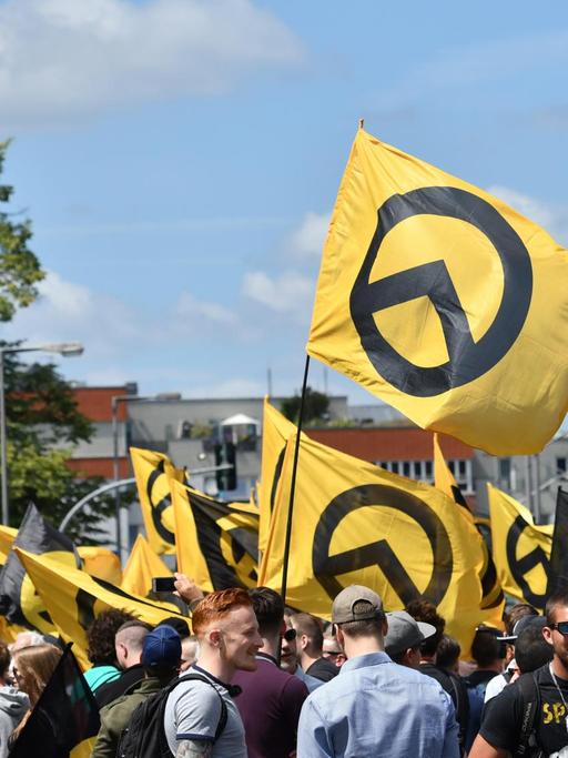 Mehrere Menschen stehen zusammen, viele von ihnen halten Fahnen hoch, auf denen das Logo der rechtsextremen "Identitären Bewegung" zu sehen ist