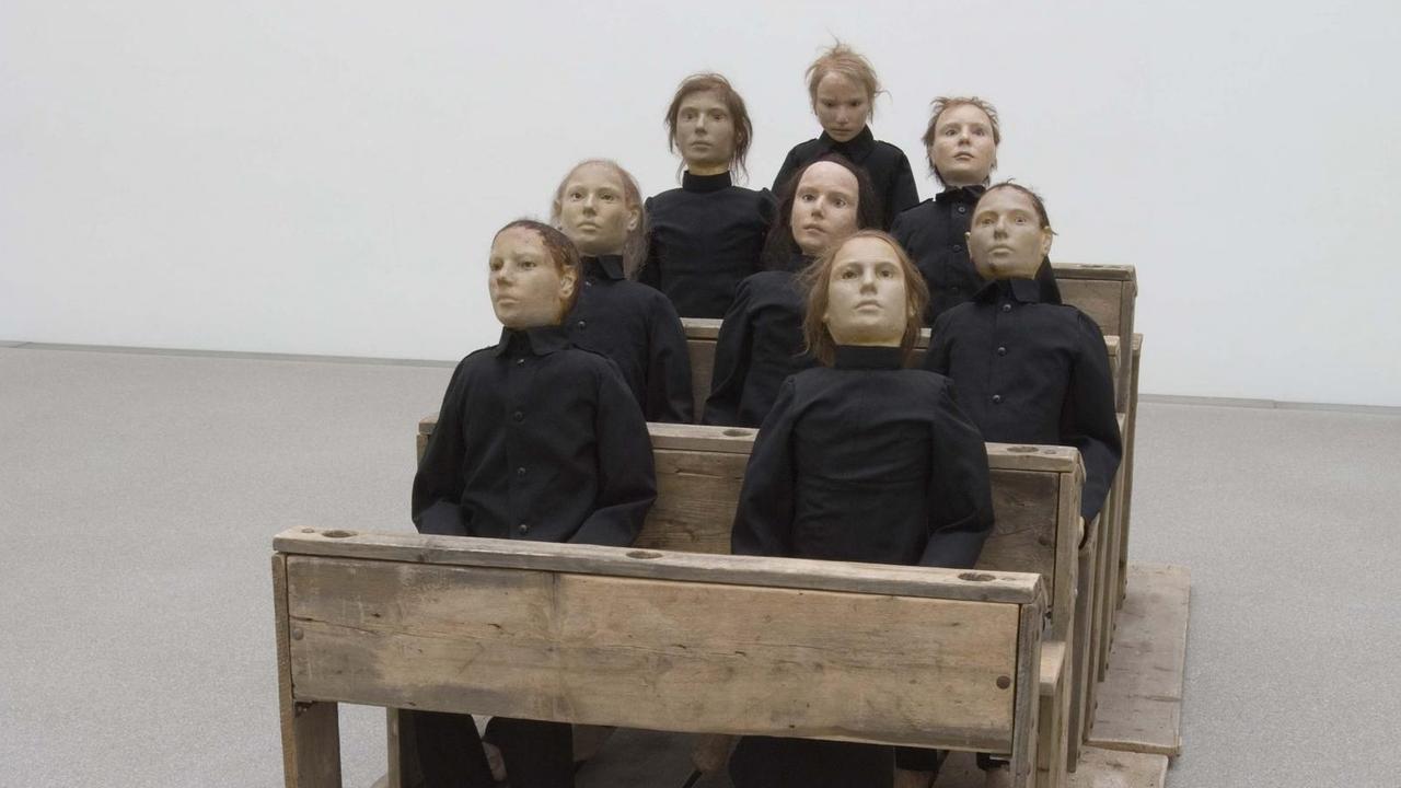 Tadeusz Kantors Kantors Arbeit "Die tote Klasse" von 1975 ist eine Rauminstallation bestehend aus Holzboden, -bänke, -tische, Puppen, und Kleidung mit einer Größe von 150 x 150 x 300cm.