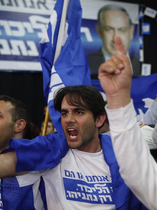 Jubelnde Parteianhänger in Wahlkampf-T-Shirts und mit Flaggen, im Hintergrund ein Plakat mit einem Bild von Benjamin Netanjahu.