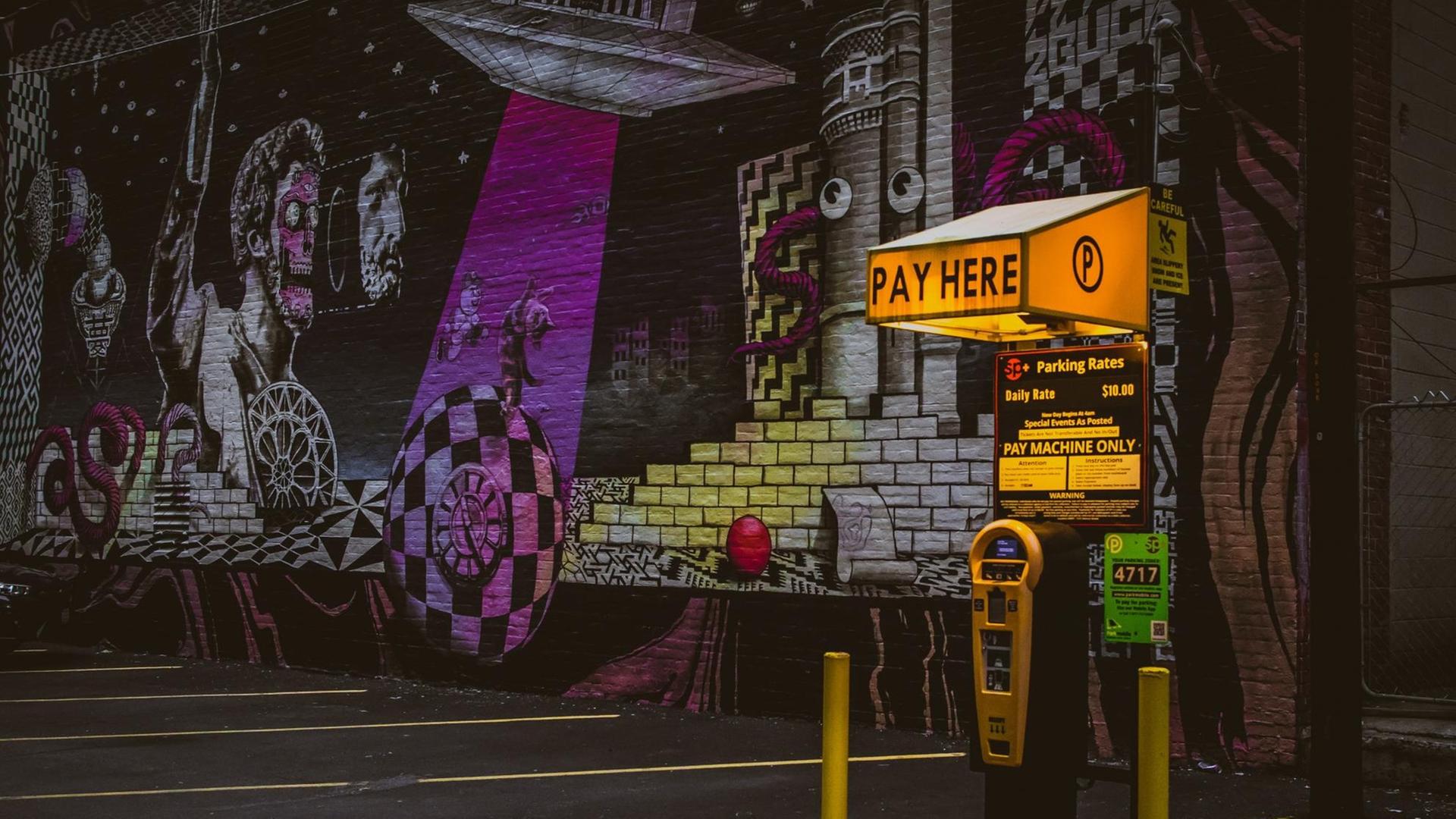 Ein Parkautomat vor einer Wand voller Graffitis.
