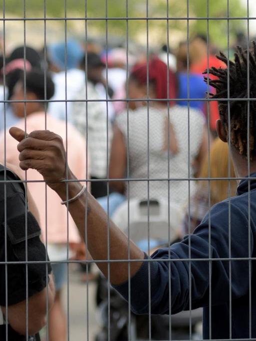 Im Transitzentrum in Manching für Asylsuchende steht ein Sicherheitsmitarbeiter neben einem Bewohner an einem Zaun.