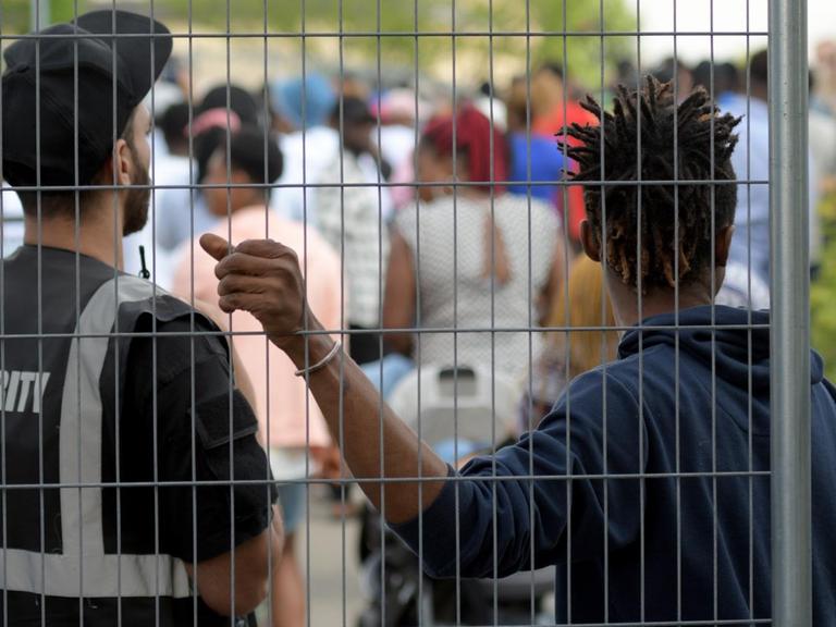 Im Transitzentrum in Manching für Asylsuchende steht ein Sicherheitsmitarbeiter neben einem Bewohner an einem Zaun.