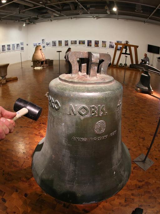 Hammer neben einer Glocke in einem Ausstellungsraum. Eine Ausstellung in Dortmund gibt Einblicke in das Glockenhandwerk.