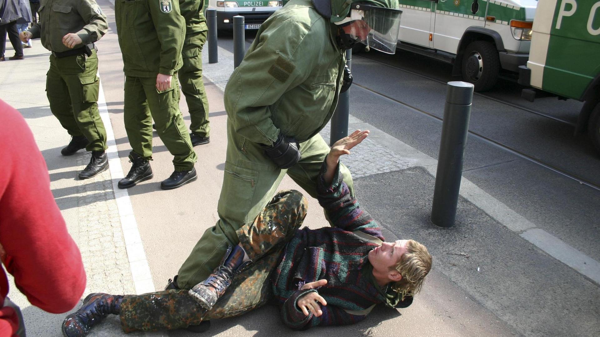 Ein Polizist steht drohend über einem Punk, der am Boden liegt.