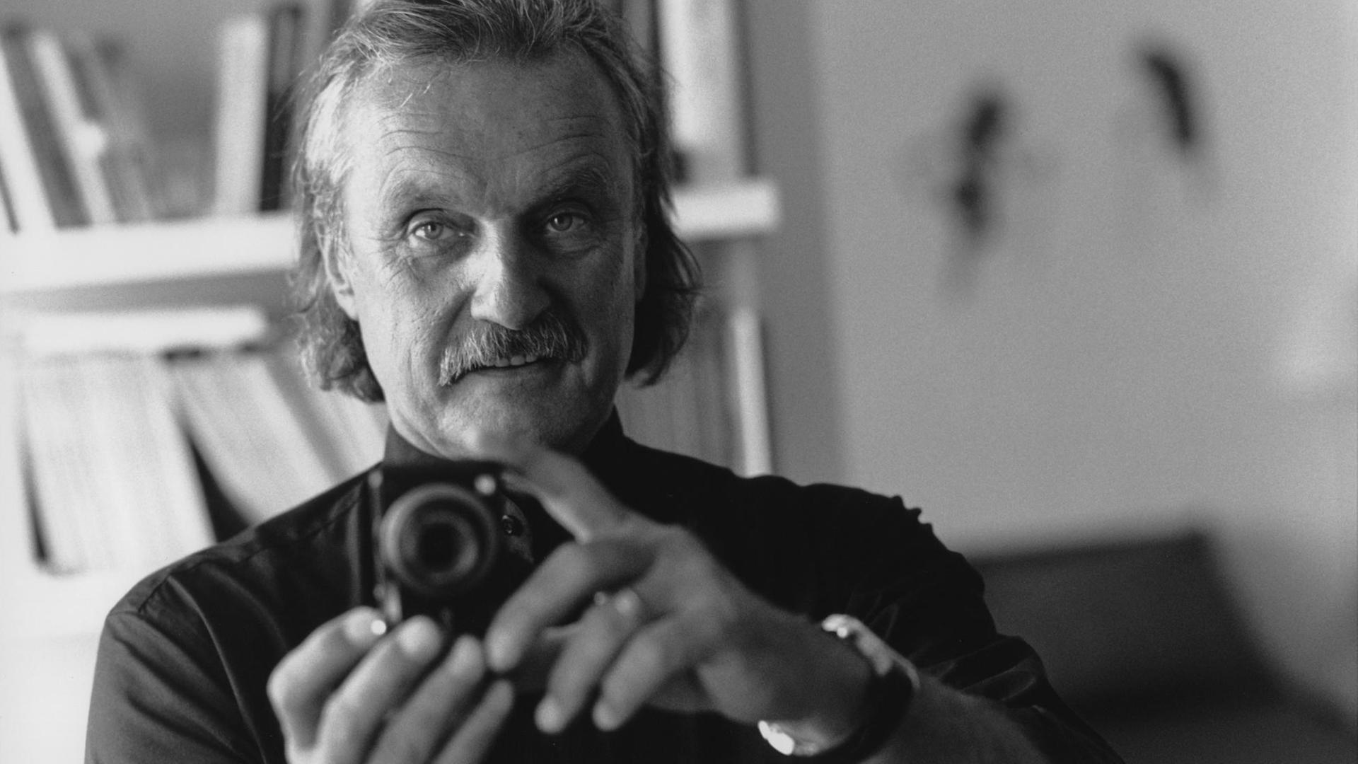 Schwarzweißfotografie zeigt den Schriftsteller Christoph Ransmayer, der eine analoge Fotokamera auf den Betrachter richtet