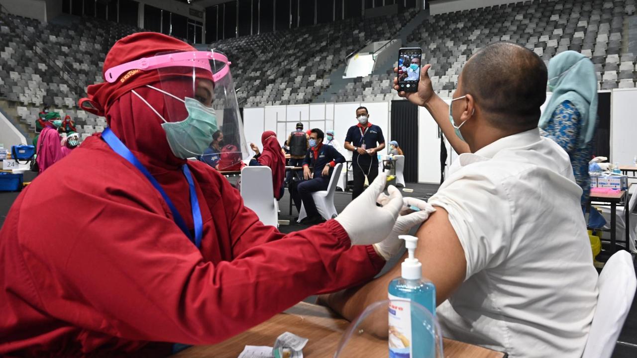 Ein Mitarbeiter des Gesundheitswesens bekommt im Stadion seine Spritze und fotografiert sich dabei