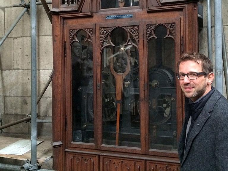 Der Kölner Dombaumeister Peter Füssenich neben dem mechanischen Uhrwerk.