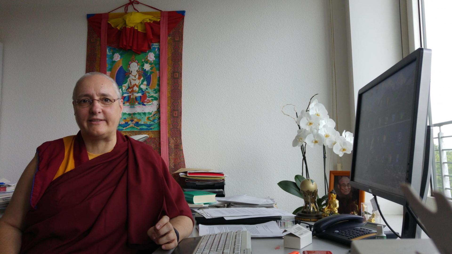 Die tibetisch-buddhistische Nonne Carola Roloff sitzt an einem Schreibtisch und blickt in die Kamera. 