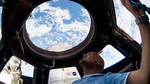 Alexander Gerst blickt in der Kuppel der Raumstation ISS durch die Fenster ins Weltall