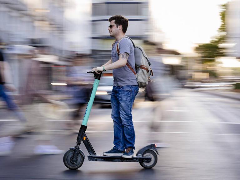Ein Mann auf einem E-Scooter fährt über die Straße.