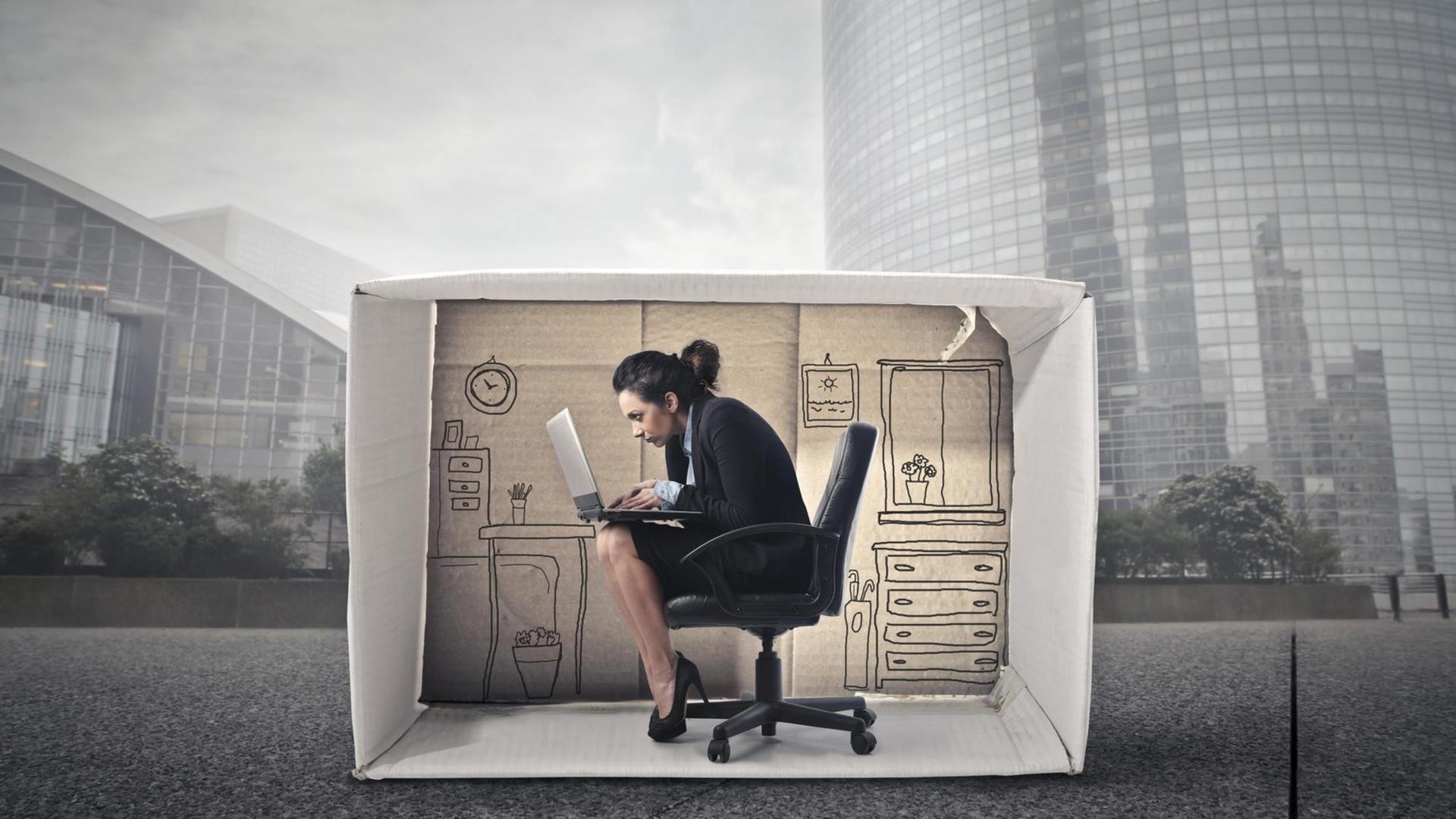 Illustration (Collage) einer Business-Frau, die in einem Karton-Büro sitzt, umgeben von einer grauen Hochhauswelt