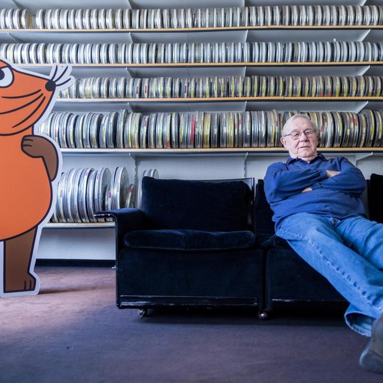Armin Maiwald, Filmemacher, Autor und Miterfinder der "Sendung mit der Maus" sitzt auf einem Sofa in seinem Büro vor zahlreichen Filmrollen. 