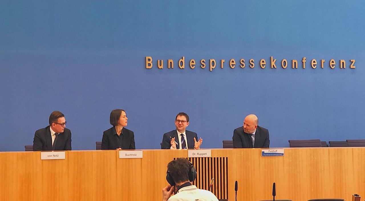 Vier Menschen mit Namensschildern hinter einem breiten Konferenztisch. Darüber die Aufschrift: "Bundespressekonferenz".