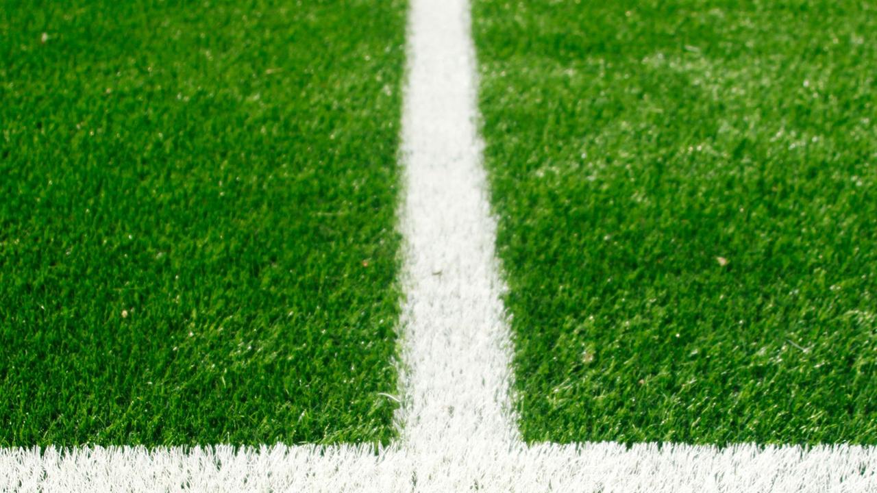 Ausschnitt von einem Fußballfeld mit weißen Linien auf grünem Rasen.