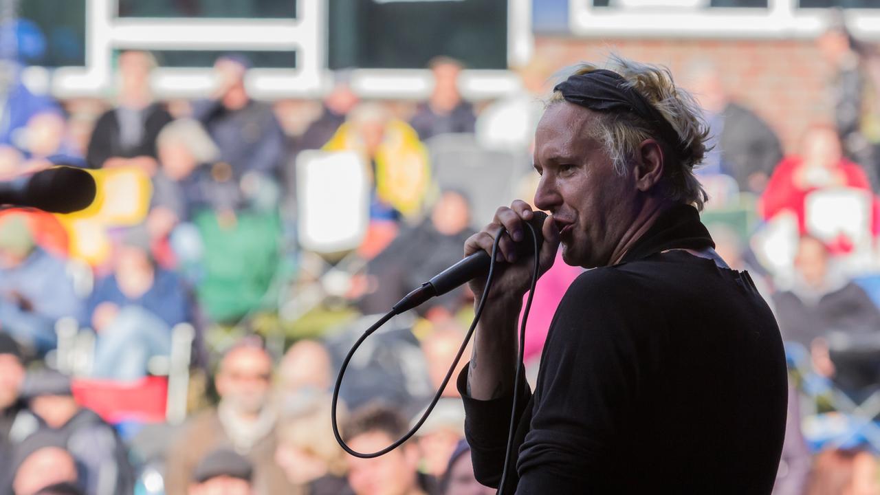 Ein Mann mit blondierten Haaren steht auf einer Bühne und singt in ein Mikrofon.