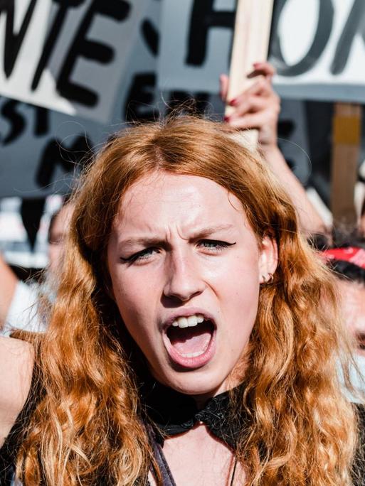 Frauendemonstration in Paris: Im Mittelpunkt des Bildes eine junge Frau mit rotblonden langen Haaren, die eine Faust in die Höhe gereckt hat. Im Hintergrund weitere in die Höhe gereckte Fäuste und Plakate.
