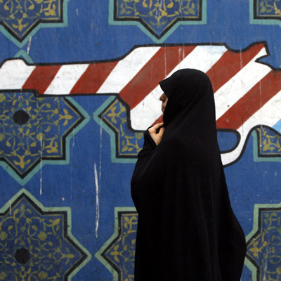 Eine Iranerin läuft vor einer Wandmalerei, das einen Revolver in den amerikanische Nationalfarben zeigt, vorbei .