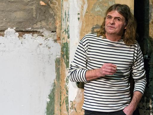 Der Musiker Wenzel mit Zigarette in der Hand vor einer heruntergekommenen Wand