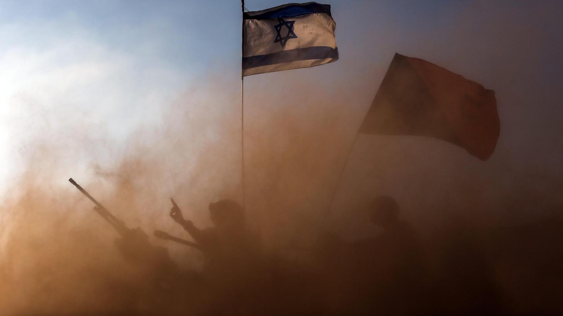 In einer Staubwolke sind die Umrisse eines Panzers und eines Soldaten zu sehen. Darüber weht die israelische Flagge.