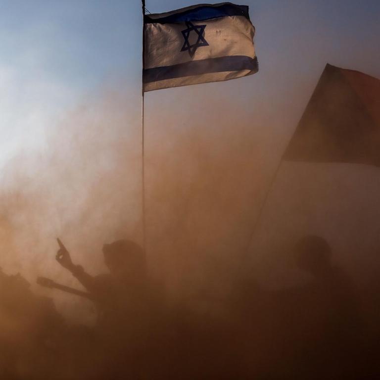 In einer Staubwolke sind die Umrisse eines Panzers und eines Soldaten zu sehen. Darüber weht die israelische Flagge.