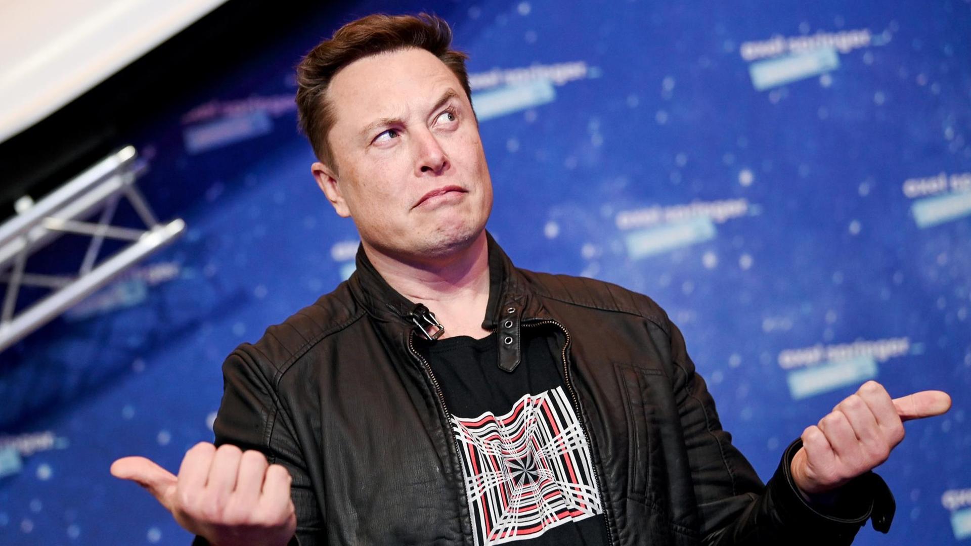 Elon Musk schaut mit hoch erhobene Augenbrauen zur Seite und gestikuliert mit seinen Händen.