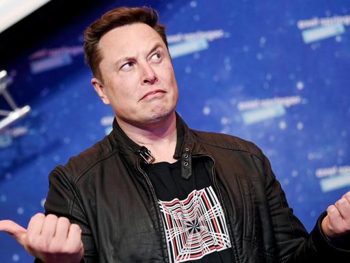 Elon Musk schaut mit hoch erhobene Augenbrauen zur Seite und gestikuliert mit seinen Händen.
