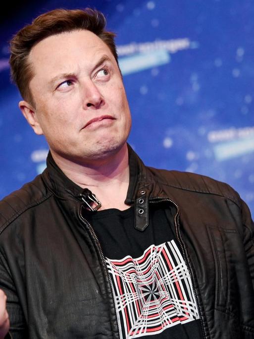 Elon Musk schaut mit hoch erhobene Augenbrauen zur Seite und gestikuliert mit seinen Händen.
