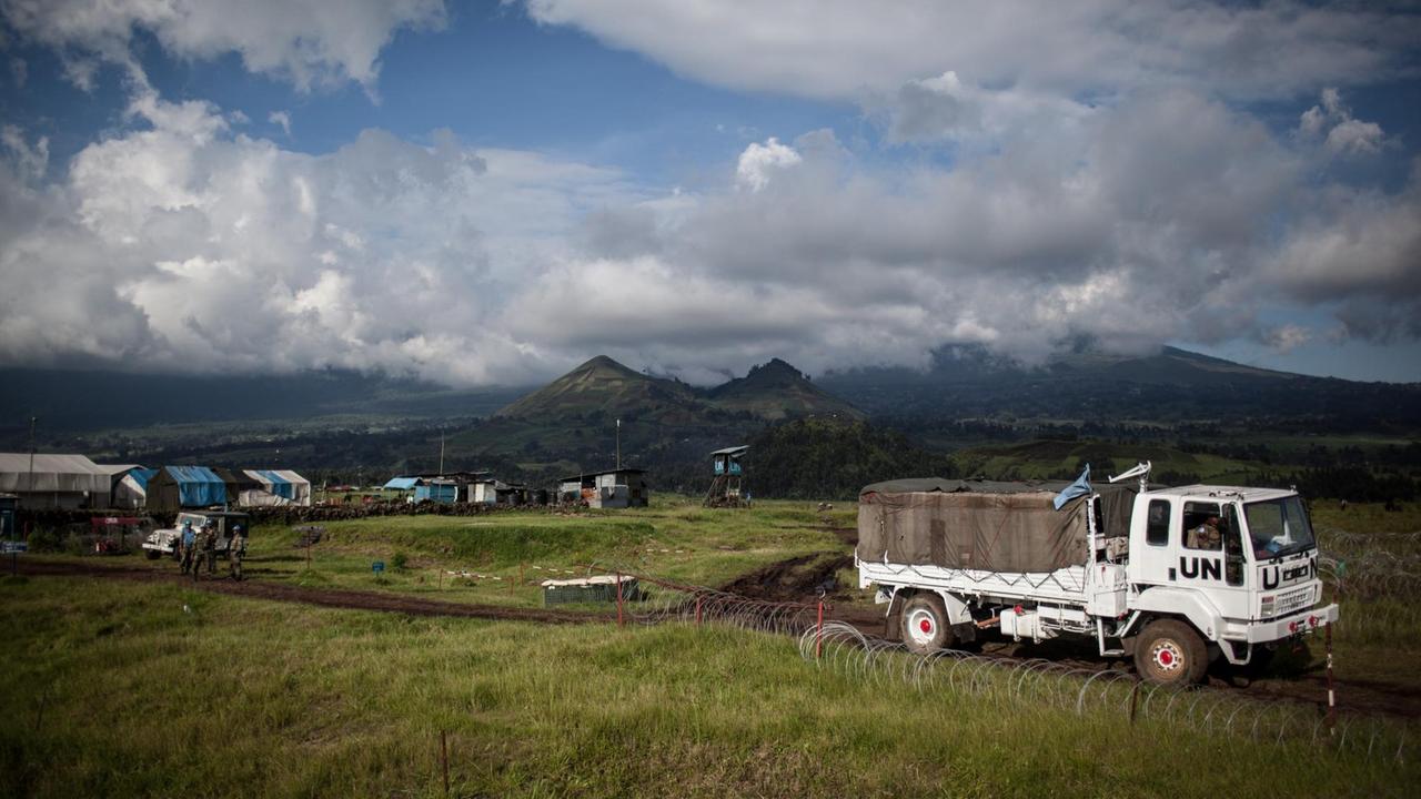 Zu sehen ist ein Lastwagen der Vereinten Nationen auf einer Wiese, im Hintergrund sind Berge und Wolken