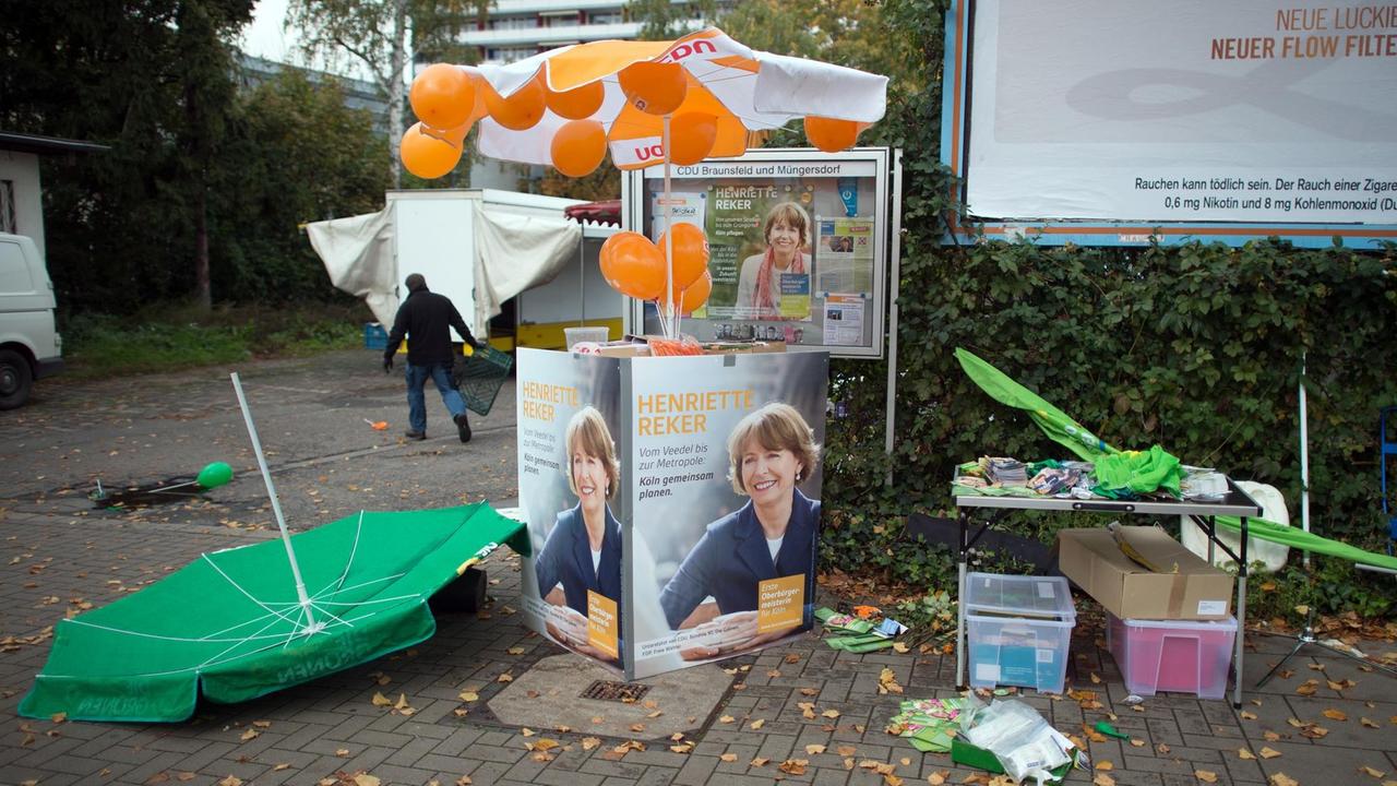 Wahlkampfmaterial und ein umgeworfener Schirm liegen vor dem Tatort, dem Stand von Henriette Reker.