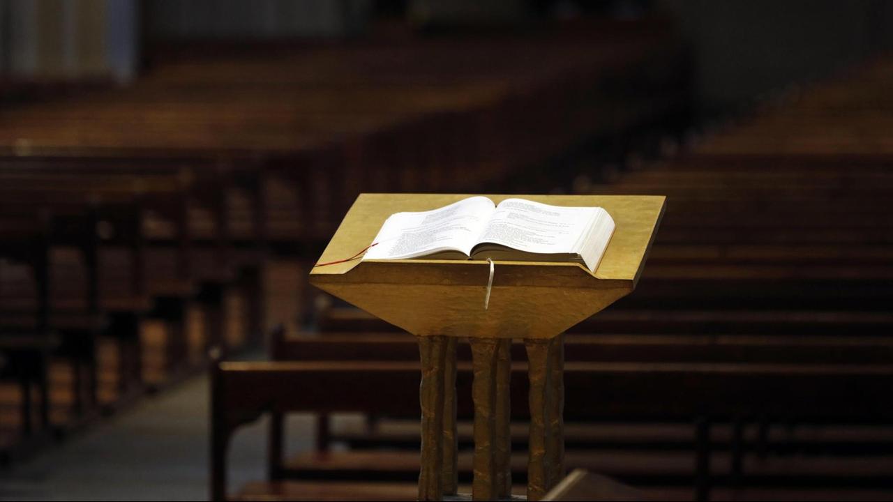 Eine Kirche im Lockdown. Eine aufgeschlagene Bibel auf einem Stehpult vor leeren Kirchenbänken.