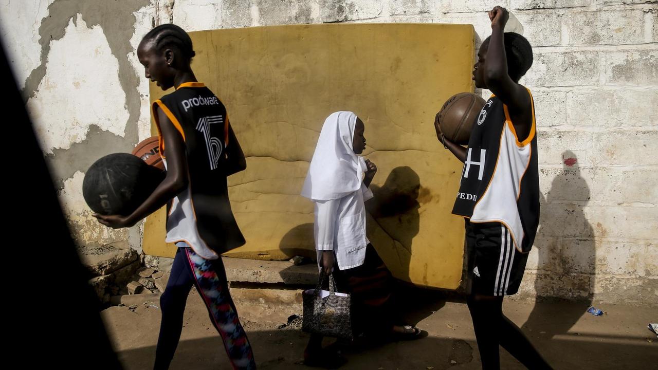 Jugendliche auf der Straße in Banjul: Zwei in Sportkleidung und ein Mädchen mit Hijab.