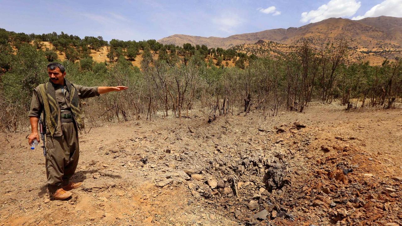 Ein PKK-Kämpfer deutet in den nordirakischen Kandil-Bergen auf einen Krater, der von einem türkischen Luftangriff stammen soll.