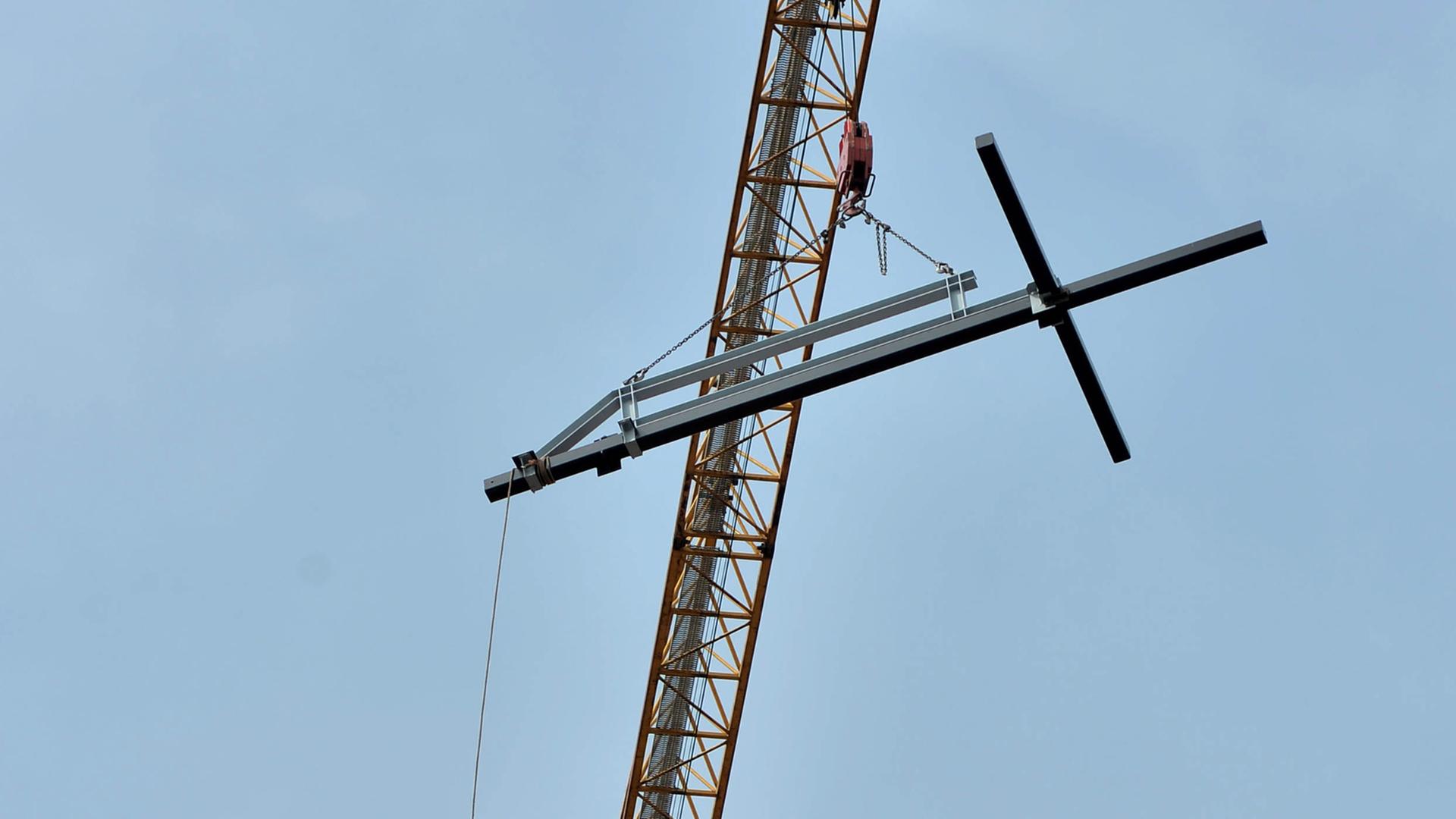 Ein christliches Kreuz hängt an einem Kran.