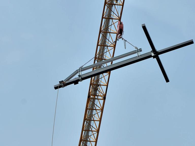 Ein christliches Kreuz hängt an einem Kran.