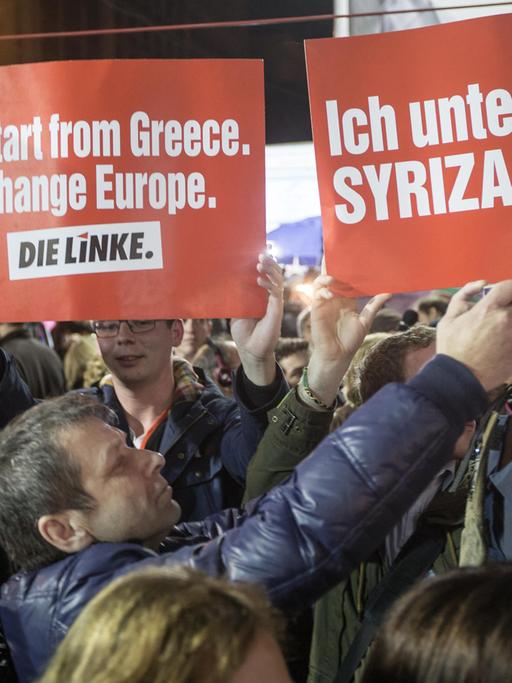 In einer Menschenmenge halten Griechen zwei Schilder der Linkspartei hoch, auf denen u.a. steht: "Ich unterstütze Syriza".