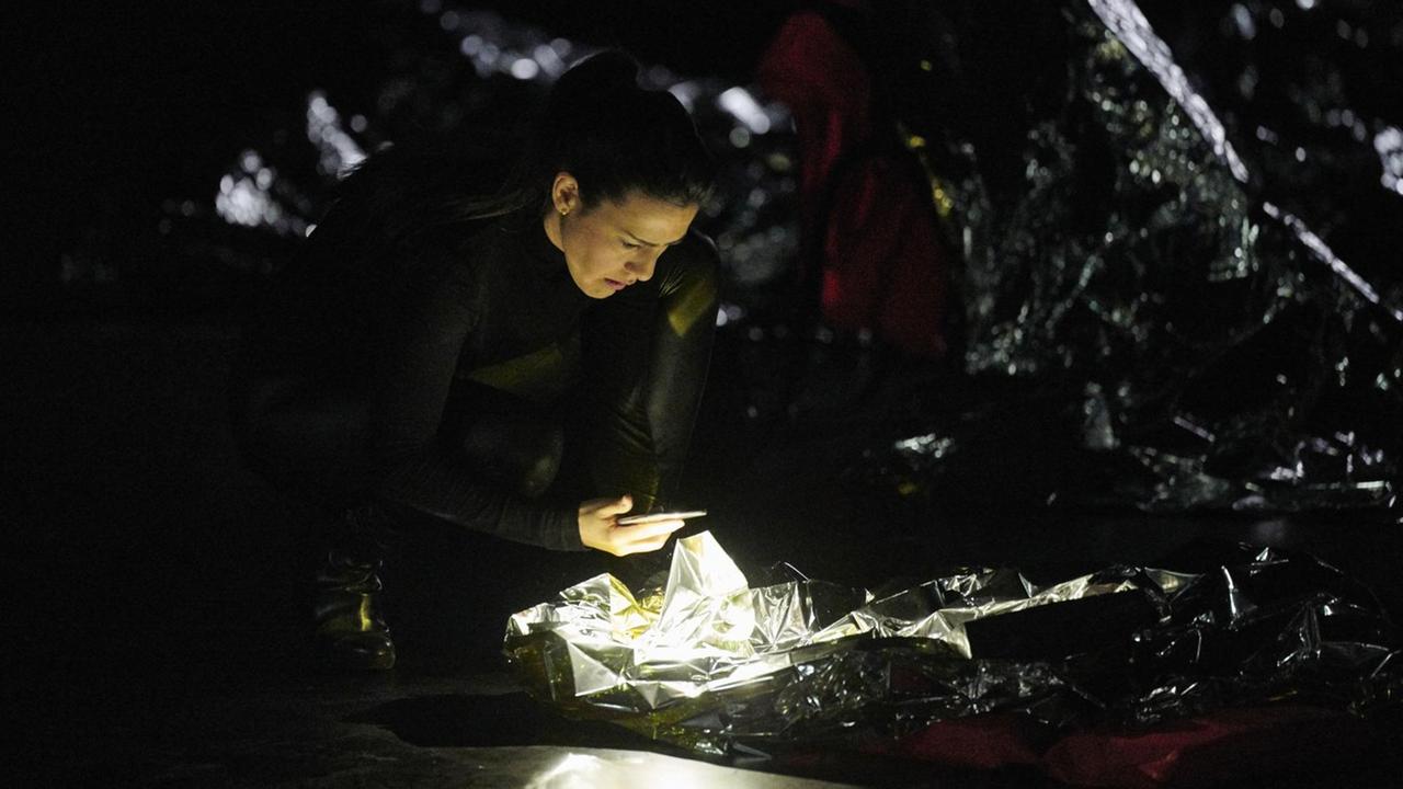 Eine Frau steht in dunkler Umgebung mit ihrem Smartphone in der Hand gebückt über einem Gebilde aus Alufolie, das hell erleuchtet ist.