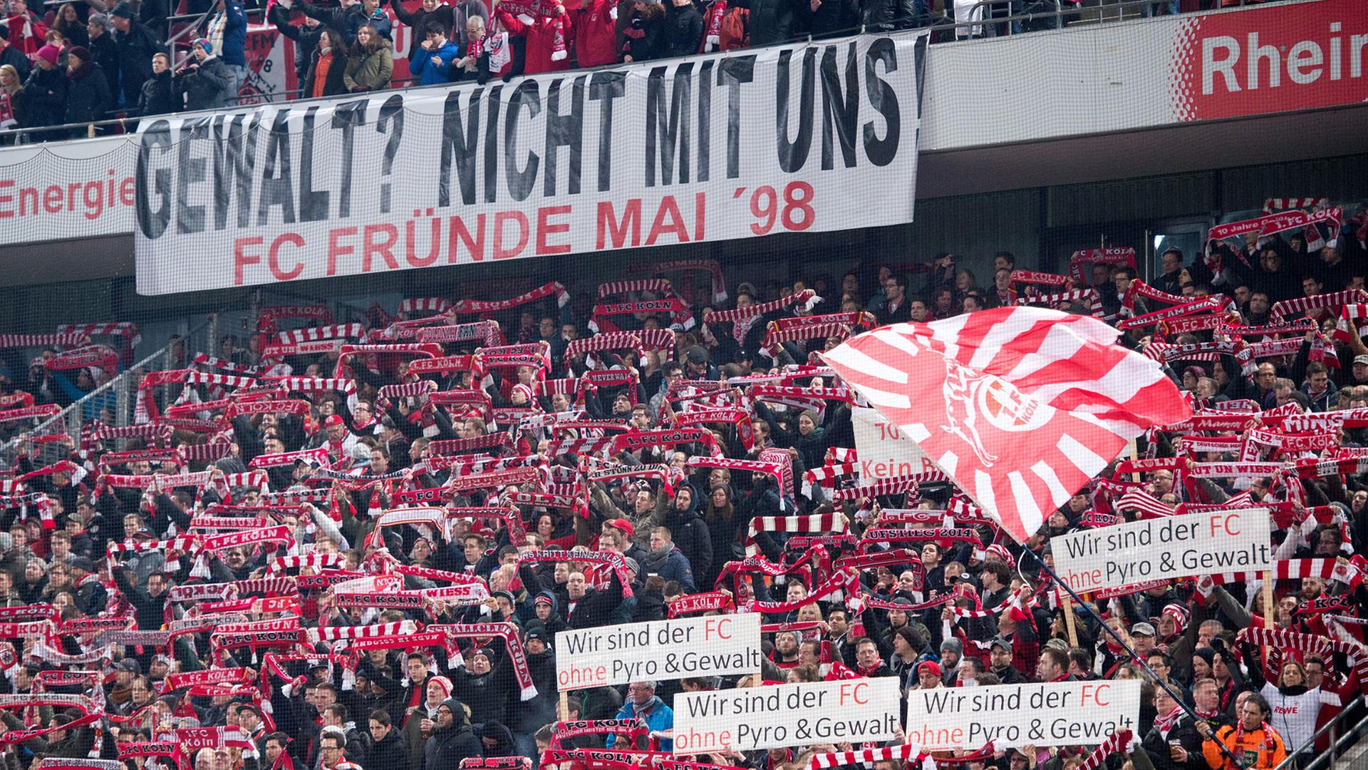 Zu sehen sind Fans vom 1. FC Köln mit Plakaten, auf denen sie sich gegen Gewalt aussprechen