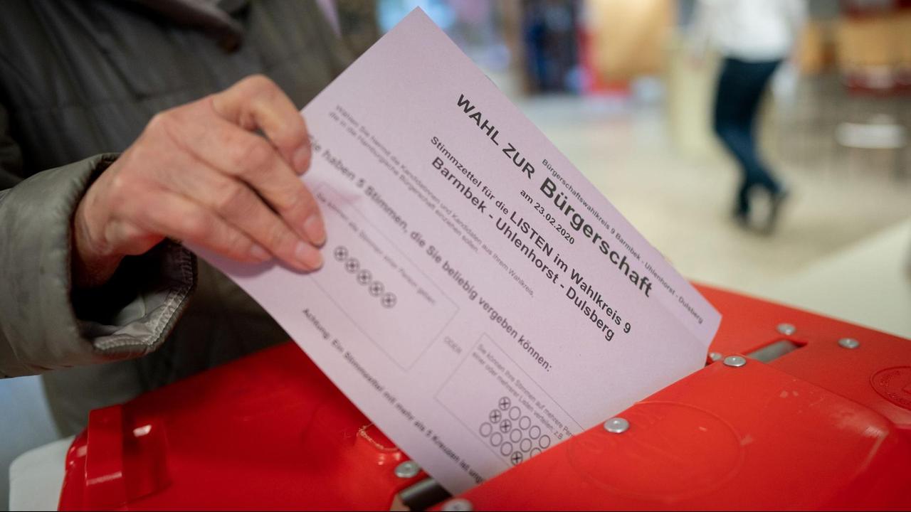 Eine Wählerin steckt ihren Stimmzettel in eine leuchtend rote Wahlurne.