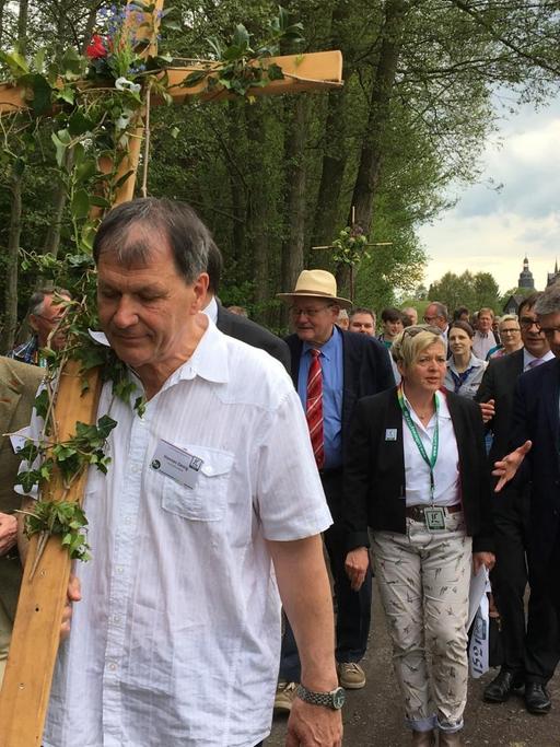 Ein Mann trägt ein Holz-Kreuz auf der Schulter. Hinter ihm läuft eine Wandergruppe. Die Gruppe pilgert auf dem neuen Lutherweg in Hessen. Foto: Deutschlandradio/Ludger Fittkau