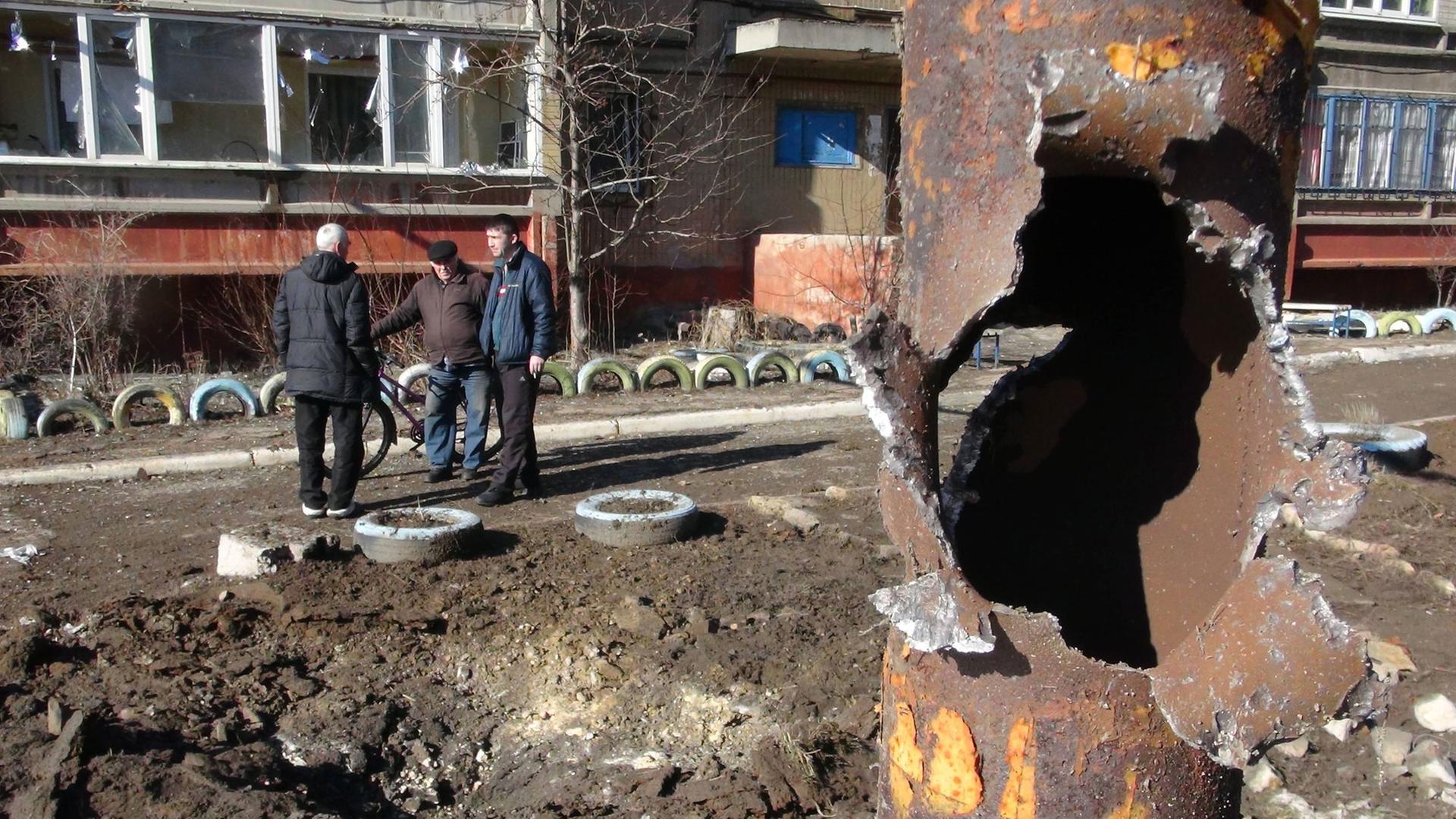 Männer stehen in einer offenbar durch Waffenbeschuss zerstörten Gegend in Donezk.