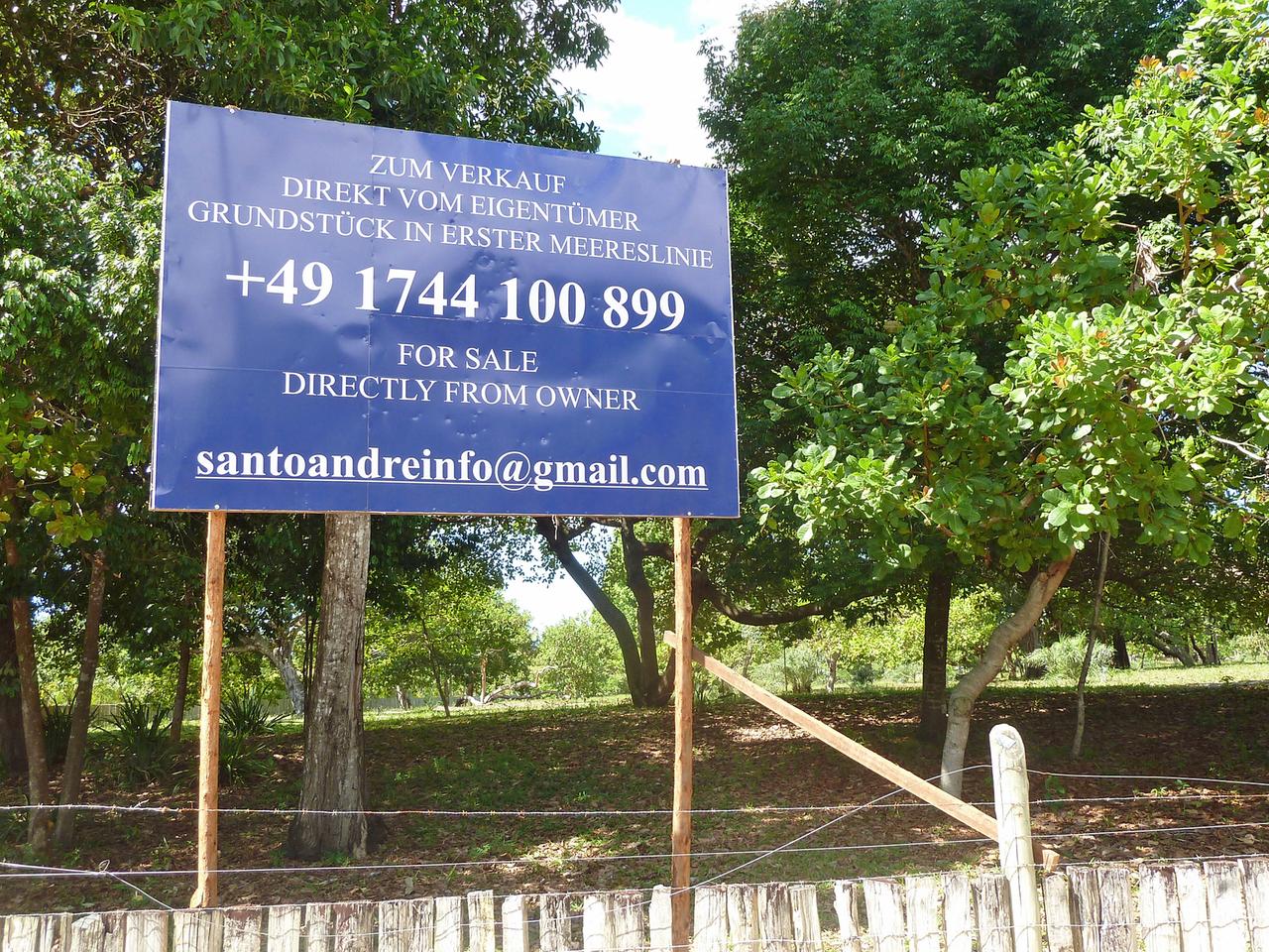 "For Sale, zum Verkauf direkt vom Eigentümer" steht auf einem blauen Schild in Santo Andre, auf dem in bestem Deutsch ein Grundstück am Strand angeboten wird.
