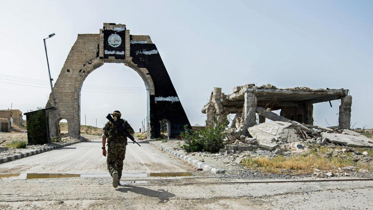 Ein kurdischer Kämpfer nähert sich einem Tor in der Nähe des Tischrin-Dammes in der syrischen Provinz Aleppo, auf dem das Logo des IS prangt, der von dort vertrieben wurde