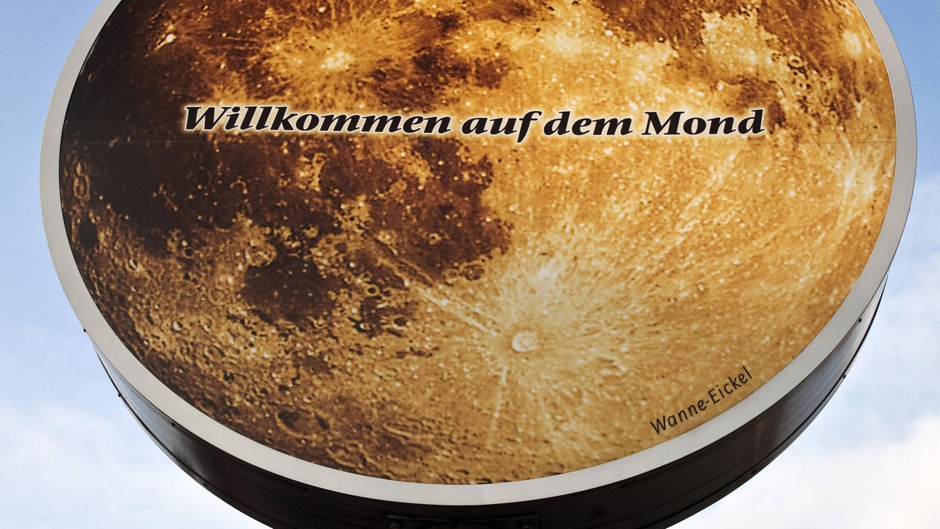 Auf einem runden Schild ist die Oberfläche des Mondes zu sehen und die Aufschrift "Willkommen auf dem Mond - Wanne-Eickel". Auf einem runden Schild ist die Oberfläche des Mondes zu sehen und die Aufschrift "Willkommen auf dem Mond - Wanne-Eickel".