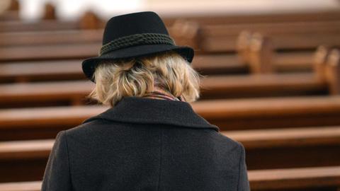 Einzelne Frau auf sonst leeren Kirchenbänken - von Generation zu Generation verliert die Kirche an Bedeutung.