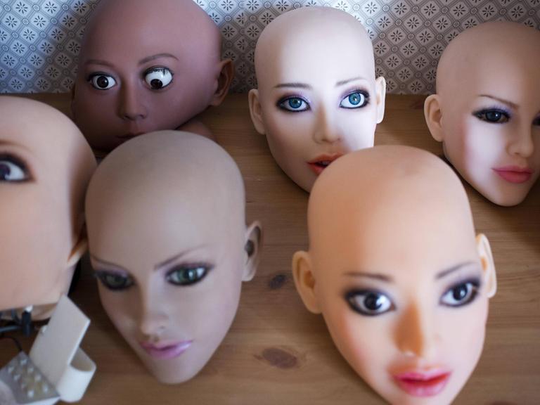 Weiblich aussehende Köpfe von Sexrobotern mit künstlicher Intelligenz stehen auf einer Holzfläche.