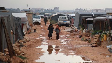 Vertriebene Syrer gehen über eine schlammige Hauptallee in einem Lager in der Nähe des Dorfes Kafr Lusin, in Idlibs nördlicher Landschaft, nahe der syrisch-türkischen Grenze.