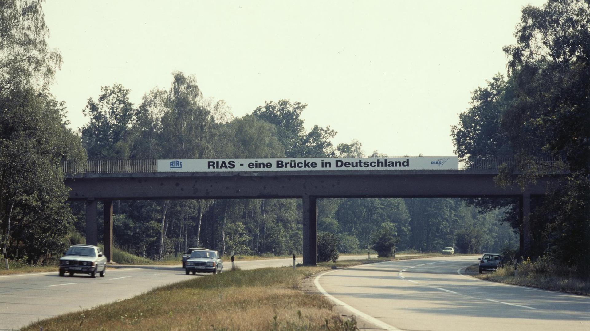 Ein Transpartent mit der Aufschrift "Rias - eine Brücke in Deutschland" ist an einer Autobahnbrücke ausgerollt.